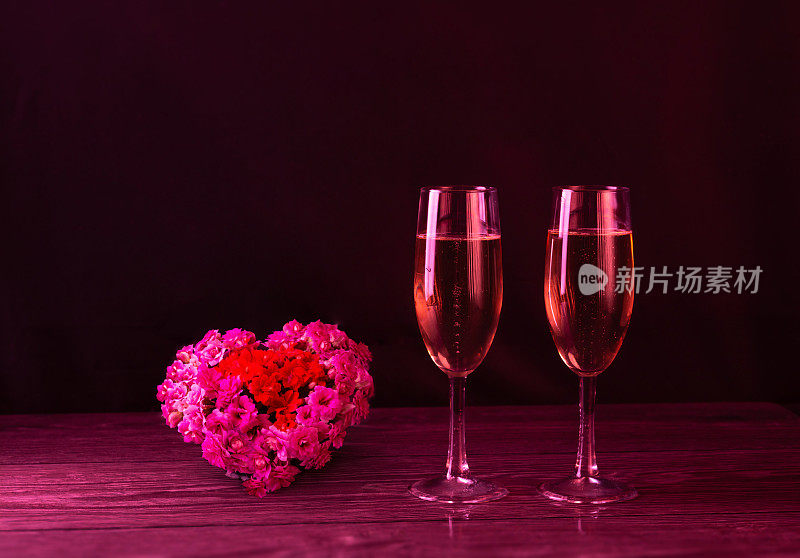 Two glasses of rosé wine. A big heart of fresh flowers on a black background. Valentine's Day. Space for text